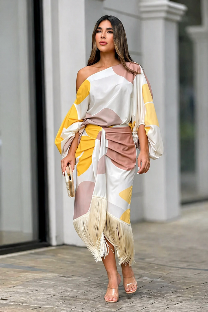 One-shoulder dress with bold yellow and mauve patterns, fringe hem, and clutch in urban setting.