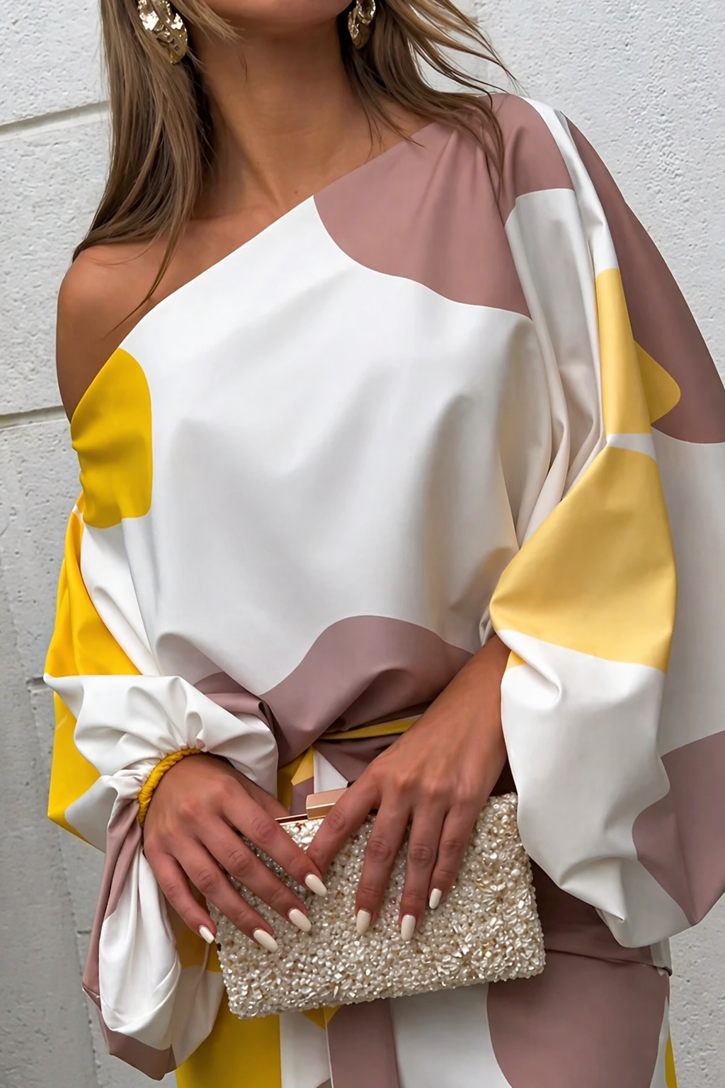 Close-up of off-shoulder dress with yellow and mauve patterns, holding beaded clutch.