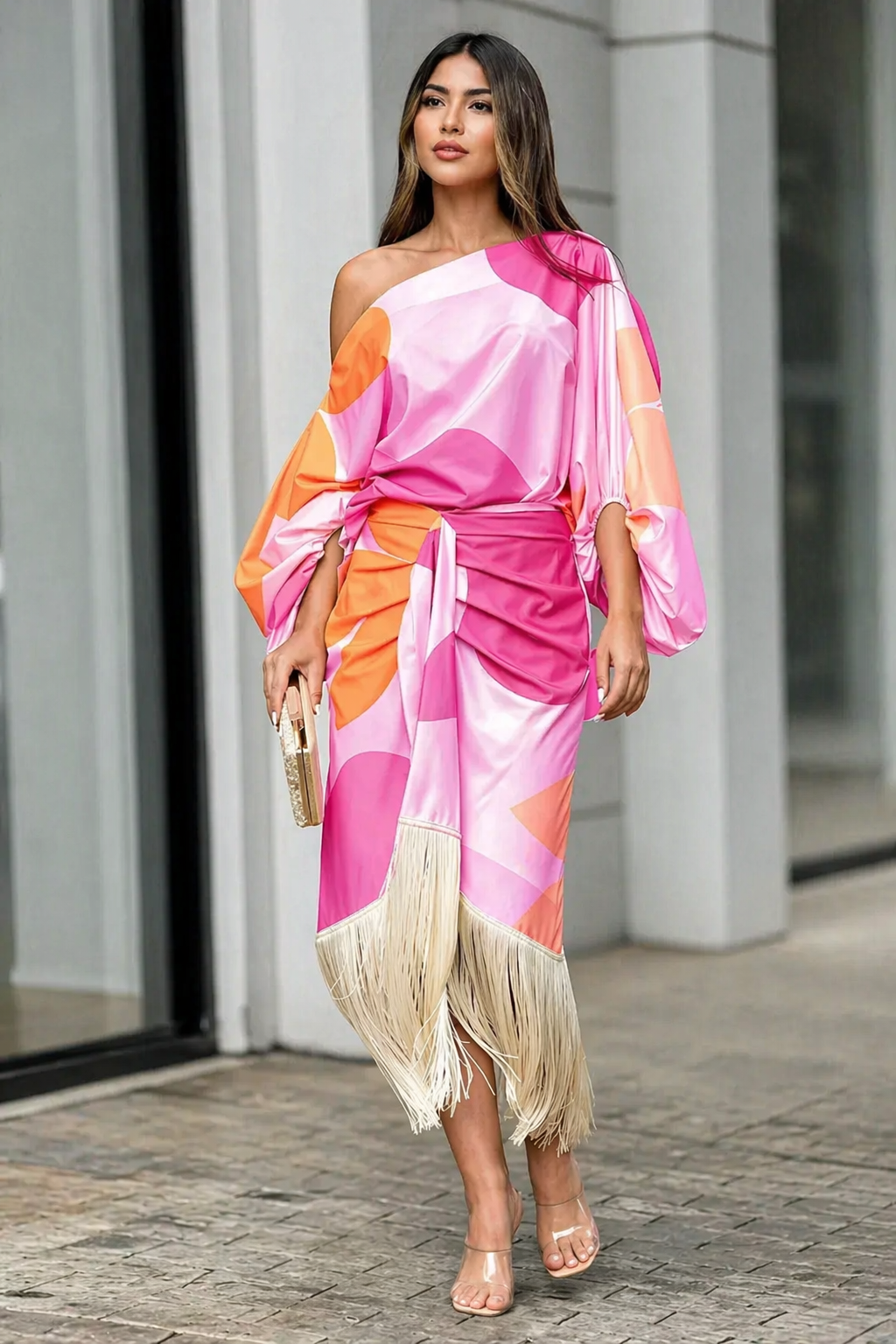 One-shoulder dress with vibrant pink and orange patterns, fringe hem, and clutch in urban setting.
