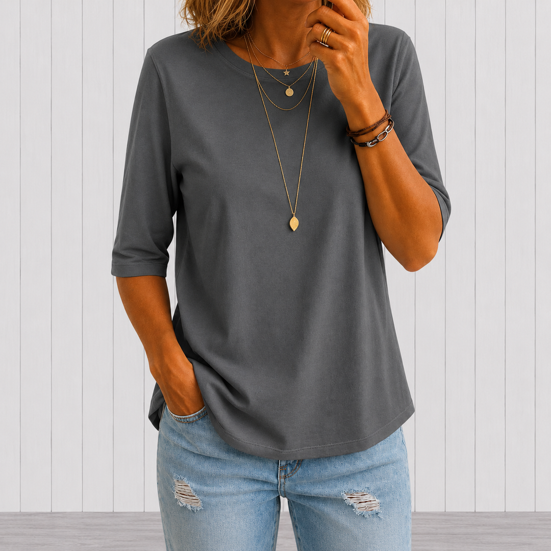 Gray three-quarter sleeve tee with layered necklaces, worn with light blue distressed jeans, against a white panel background.