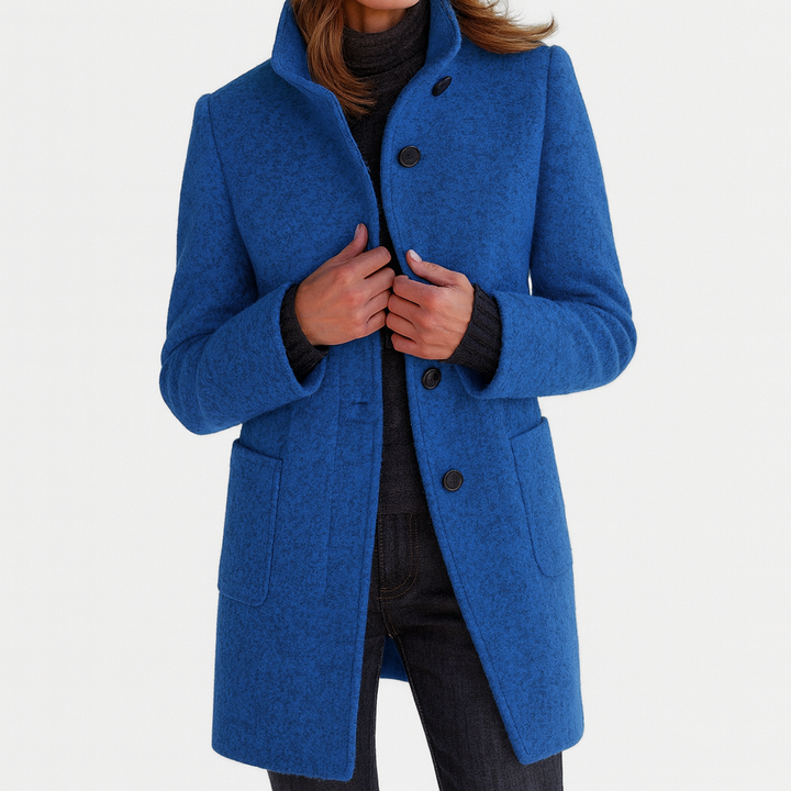 Vibrant blue elegant coat with high collar and button closure, worn by model with dark turtleneck and pants in studio setting.