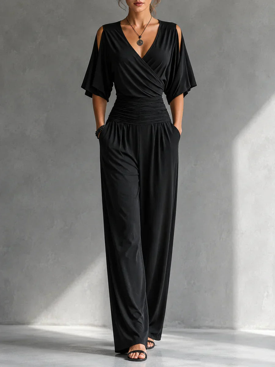 Woman wearing a black elegant jumpsuit with cutout shoulders and ruched waist in a gray studio setting.
