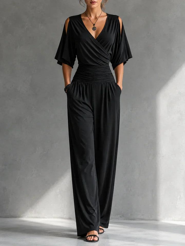 Woman wearing a black elegant jumpsuit with cutout shoulders and ruched waist in a gray studio setting.