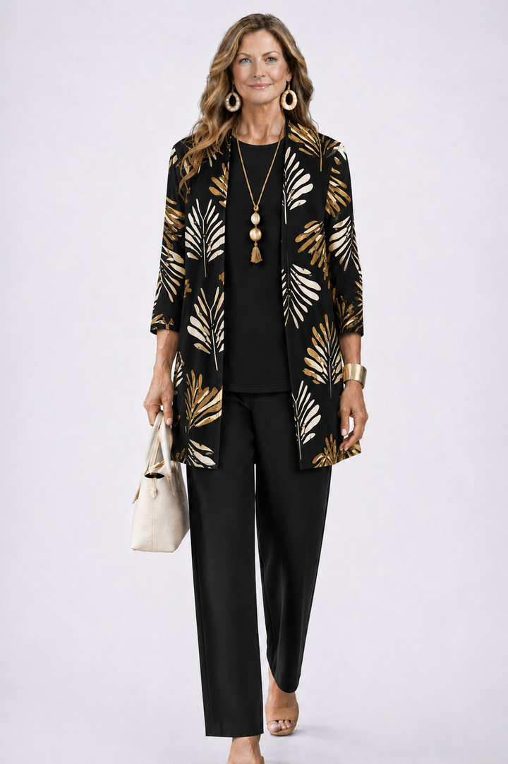 Woman in a black three-piece set with a gold leaf pattern cardigan. White studio background.