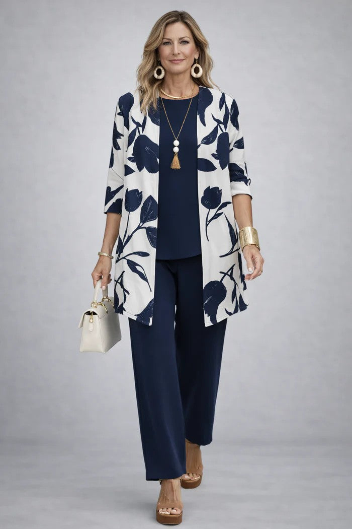 Woman wearing a navy blue and white floral three-piece outfit. Grey studio setting.