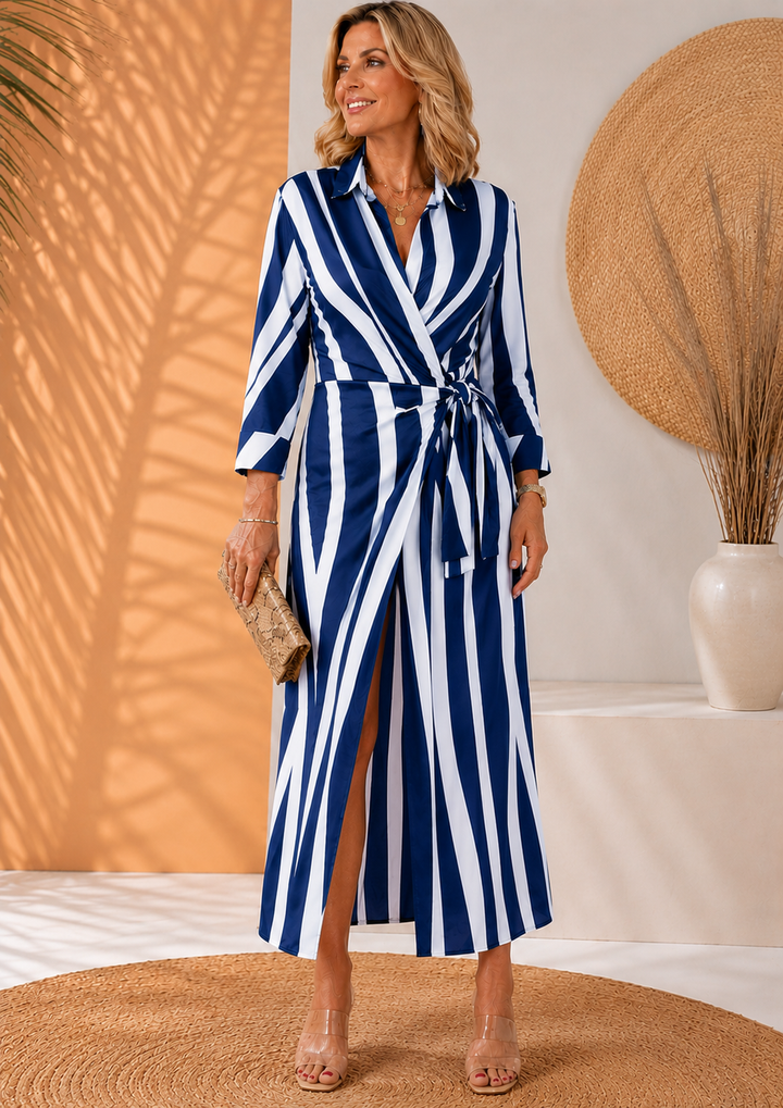 Model in navy-white striped maxi dress, holding clutch, on woven rug with earthy decor.
