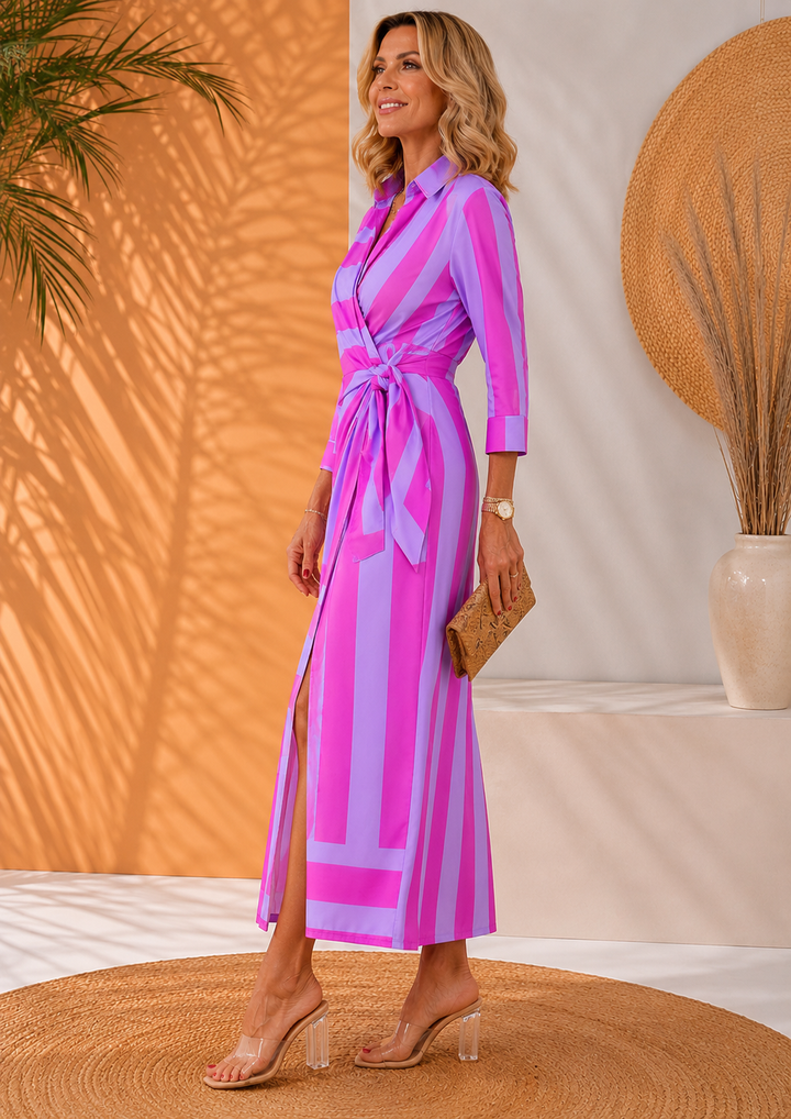 Side view of model in purple-pink striped maxi dress, holding clutch on woven rug.