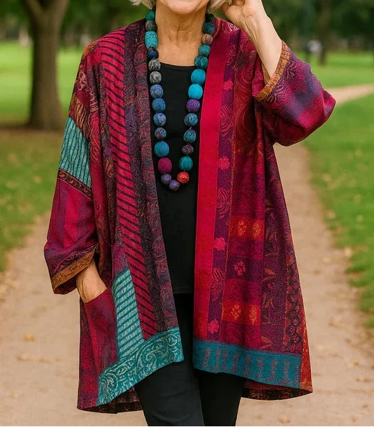 Woman modeling a vibrant red and blue drape cardigan with intricate patterns, standing on a park walkway.