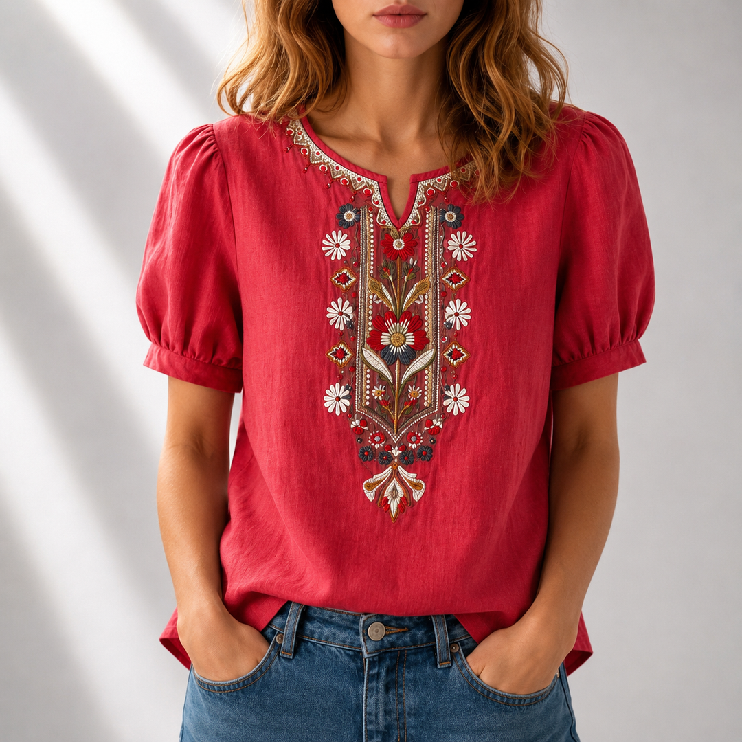 Woman in a red blouse with colorful floral embroidery, puff sleeves, in a softly lit studio.