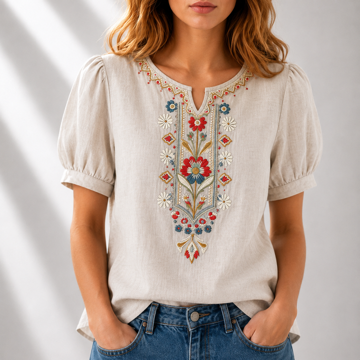 Woman wearing a beige blouse with colorful floral embroidery, puff sleeves, in a light studio setting.