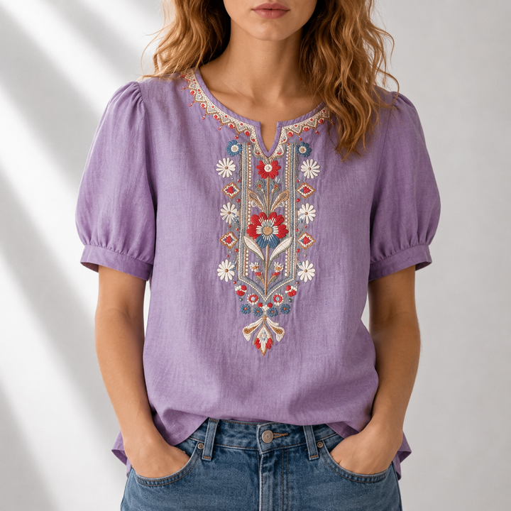 Woman wearing a purple blouse with detailed floral embroidery, puff sleeves, in a bright studio environment.