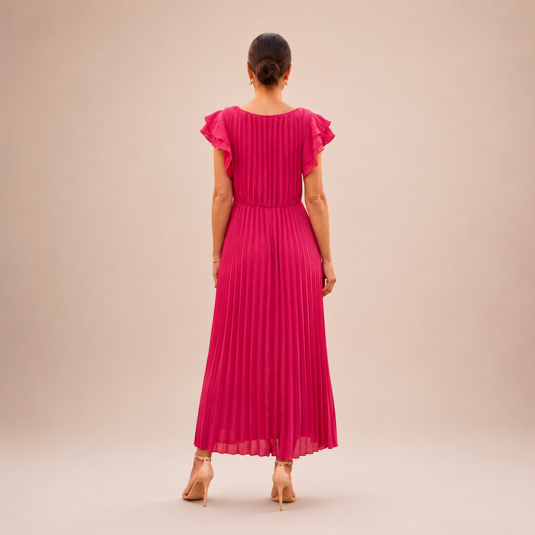 Back view of a woman in a pink pleated maxi dress with ruffle sleeves in a studio setting.