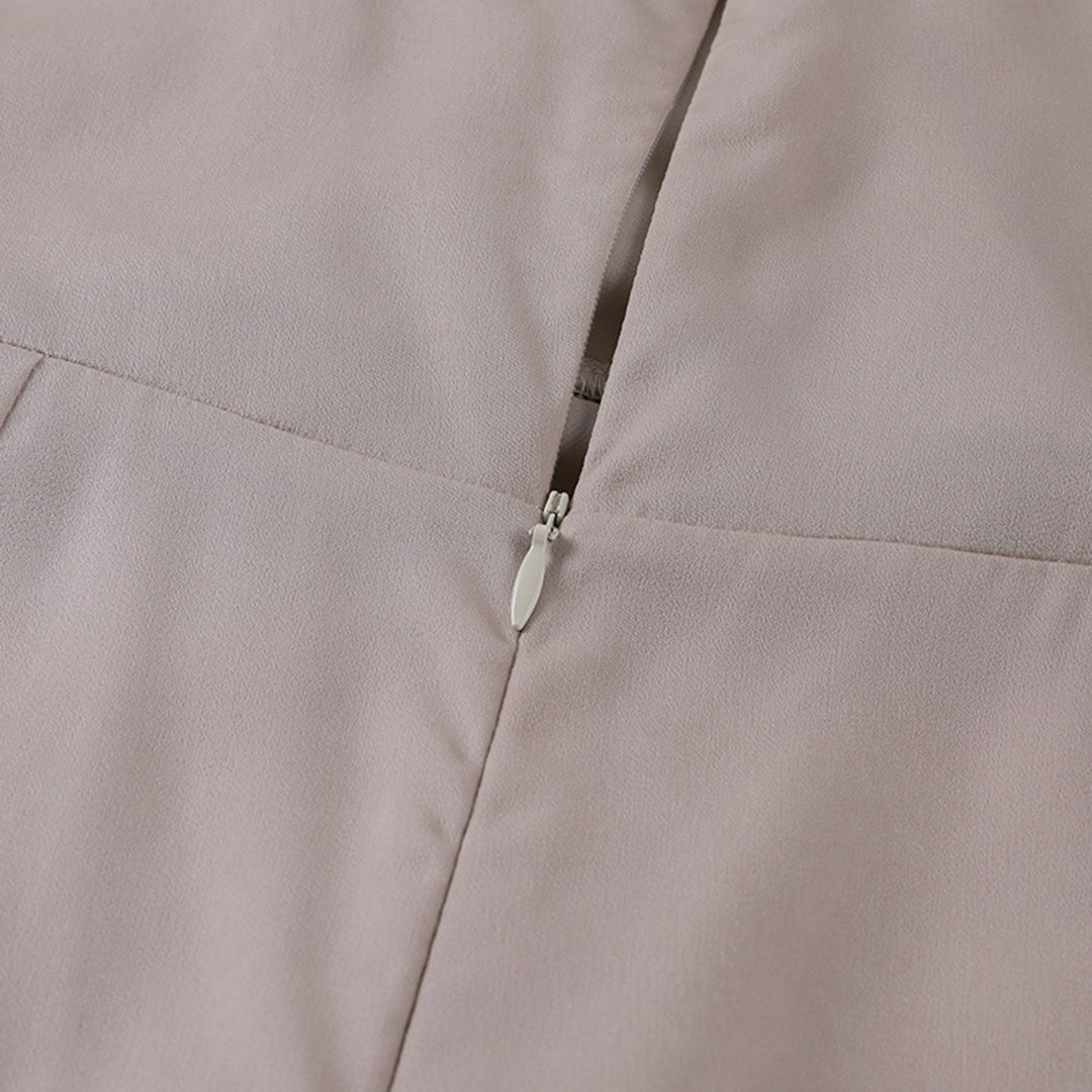 Close-up of a light beige dress showcasing the zipper detail in a studio setting.