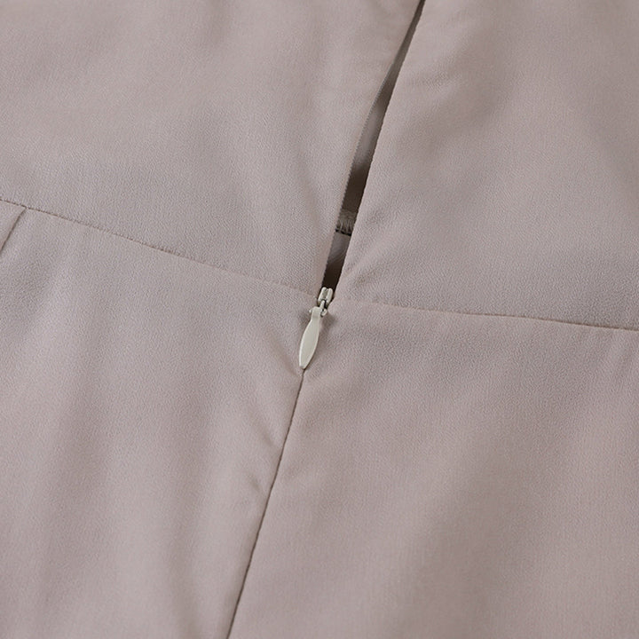 Close-up of a light beige dress showcasing the zipper detail in a studio setting.