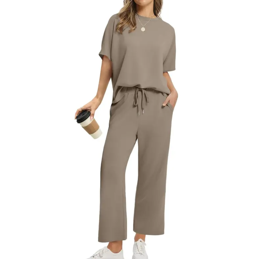 Woman in a fashionable taupe set with loose top and drawstring pants, holding a coffee, in a studio environment.