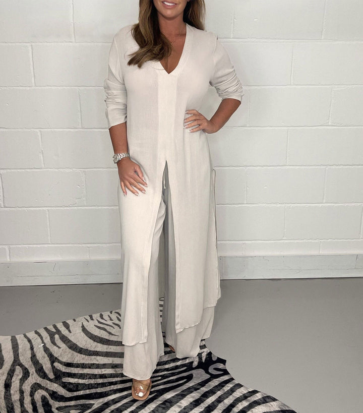 Model in a light gray two-piece set with long sleeves and a V-neck, standing on a zebra-patterned rug against a white brick wall.
