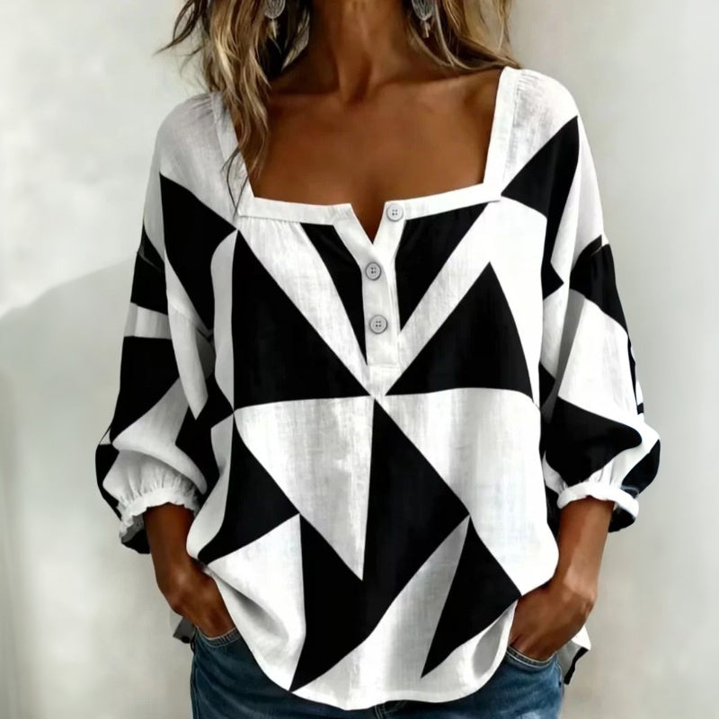 Casual geometric blouse in black and white with button details, worn by model with hands in pockets, studio background.