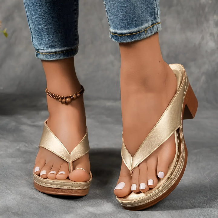 Gold high-heeled mule worn, paired with rolled-up jeans, and anklet, on a carpeted floor.