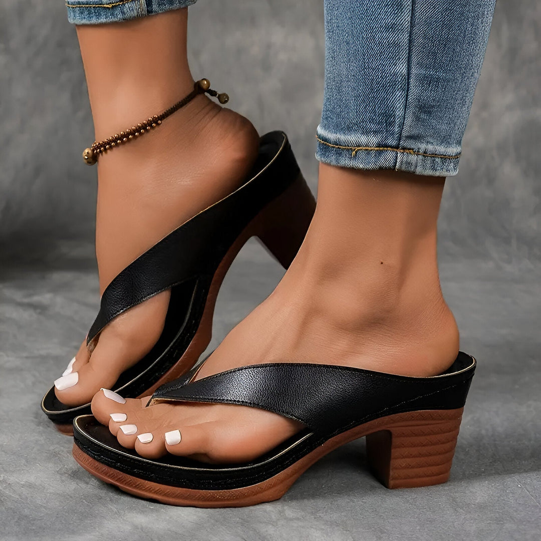 Black high-heeled mule worn with jeans and anklet, showing elegant design against a gray background.