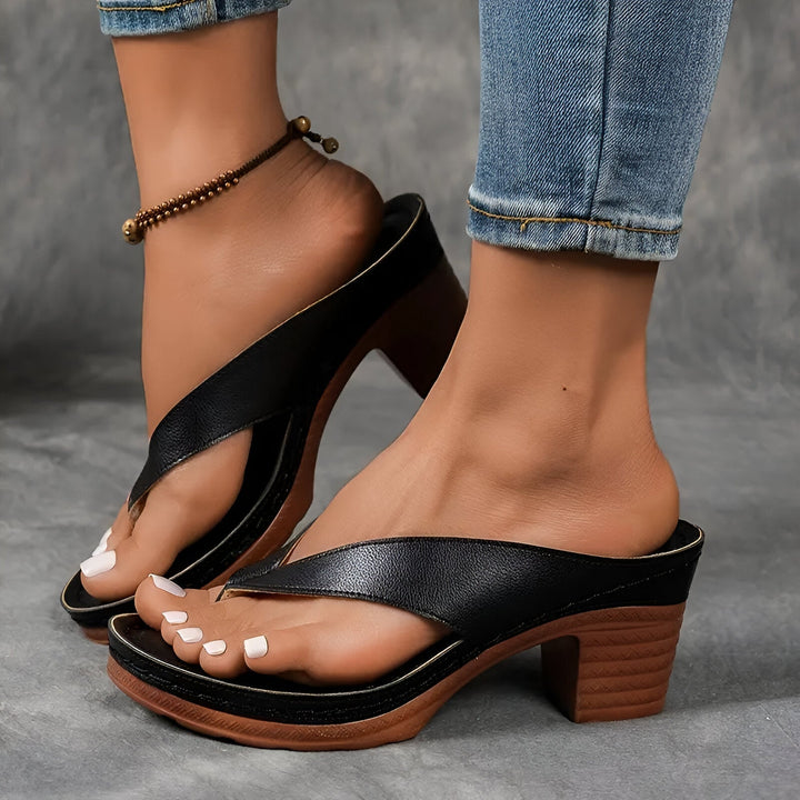 Black high-heeled mule worn with jeans and anklet, showing elegant design against a gray background.