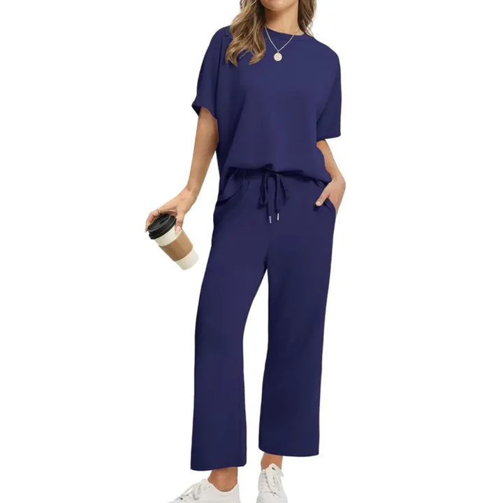 Woman wearing a stylish navy set with loose top and drawstring pants, holding a coffee, in a studio setting.
