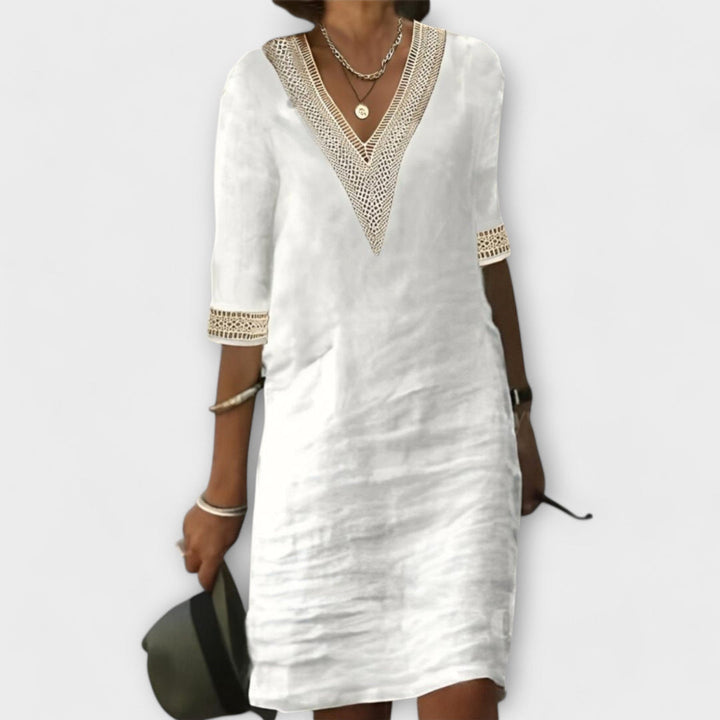 White elegant dress with V-neck and lace trim, styled with silver jewelry against a plain background.