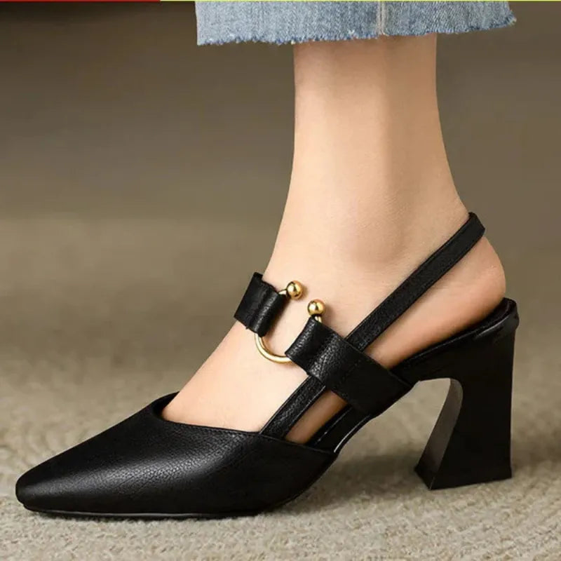 Black heel with gold accents on foot in indoor setting, paired with light denim.