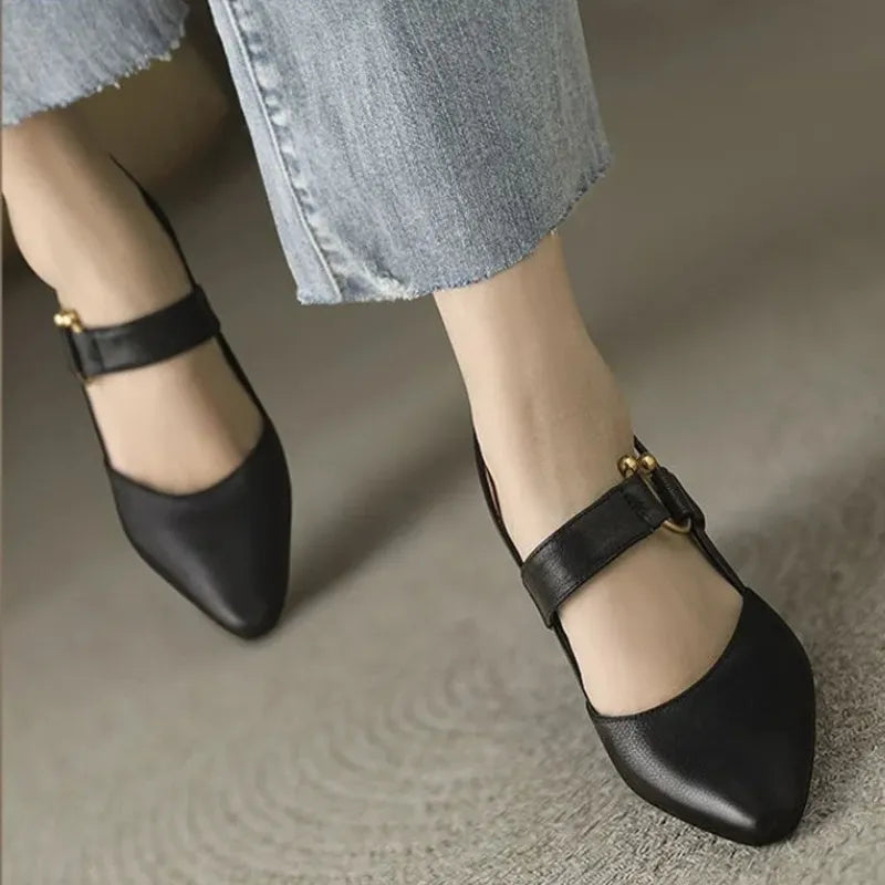 Black heels with gold accents on feet on carpet, paired with light denim.