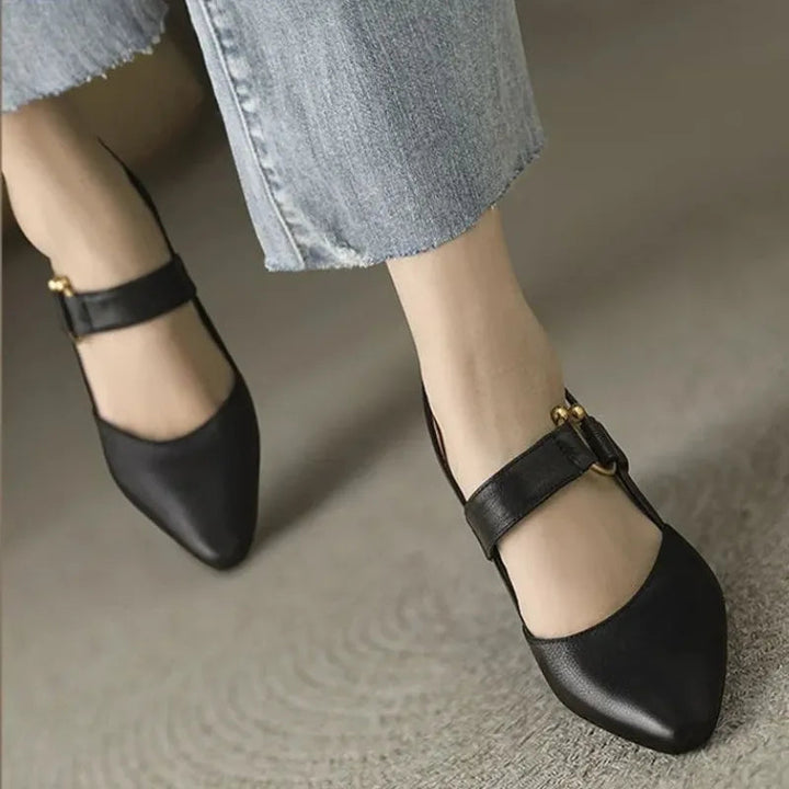 Black heels with gold accents on feet on carpet, paired with light denim.