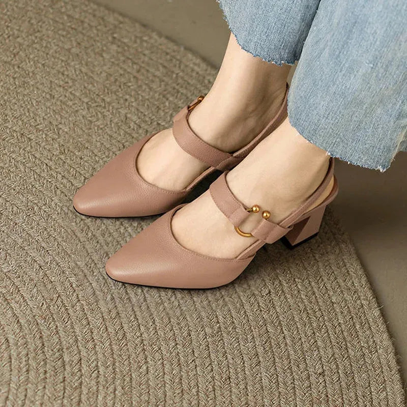 Beige heels with gold accents on feet on carpet, paired with light denim.