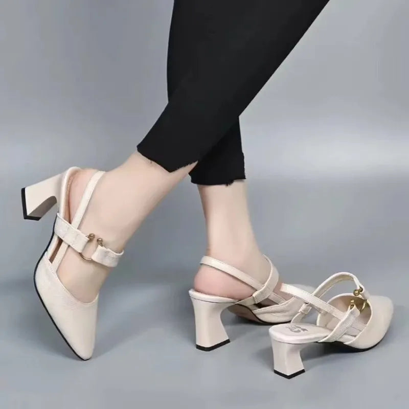 White heels with gold accents on crossed legs in studio setting, paired with black pants.