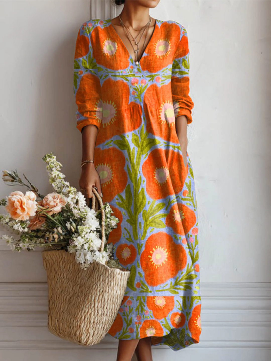 Woman wearing a vintage floral pattern dress with red-orange flowers and green leaves, holding a woven basket with flowers, set against a simple indoor background.