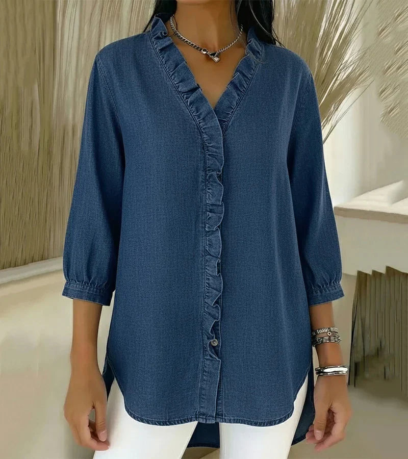 Elegant denim blouse with ruffled trim in blue, worn by model indoors against a neutral background.