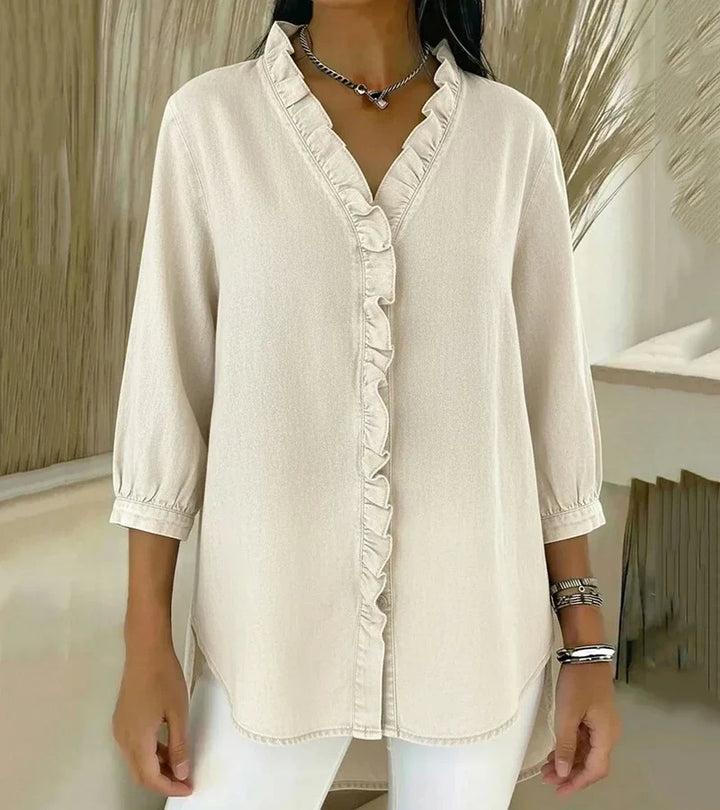 Cream denim blouse with elegant ruffled front and 3/4 sleeves, styled with white pants indoors.