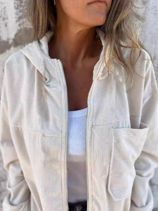 Beige corduroy zip jacket worn over a white top, featuring a relaxed fit and visible pocket stitching, set against a textured wall backdrop.
