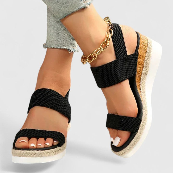 Black platform orthopedic sandals worn with light jeans and a gold chain anklet, displayed in a studio.