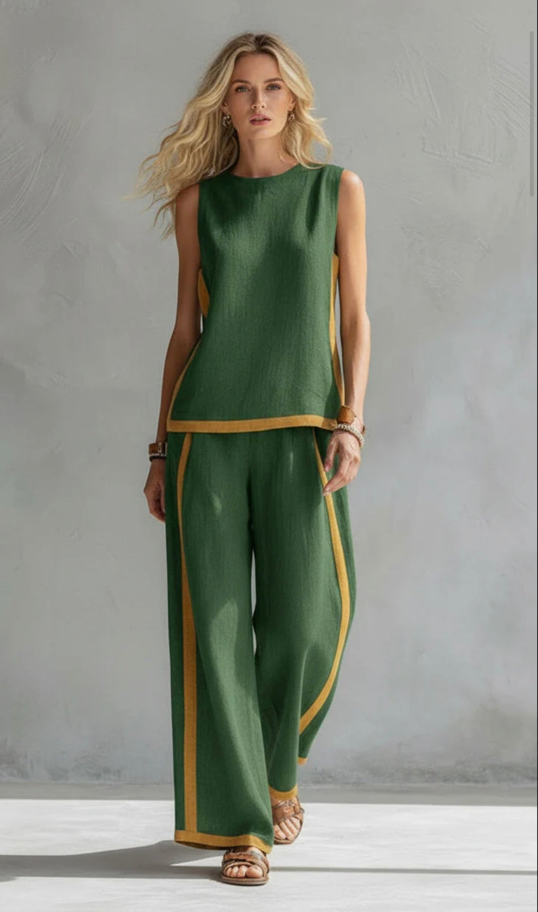 Model wearing a green two-piece set with yellow trim, standing in a gray textured studio.