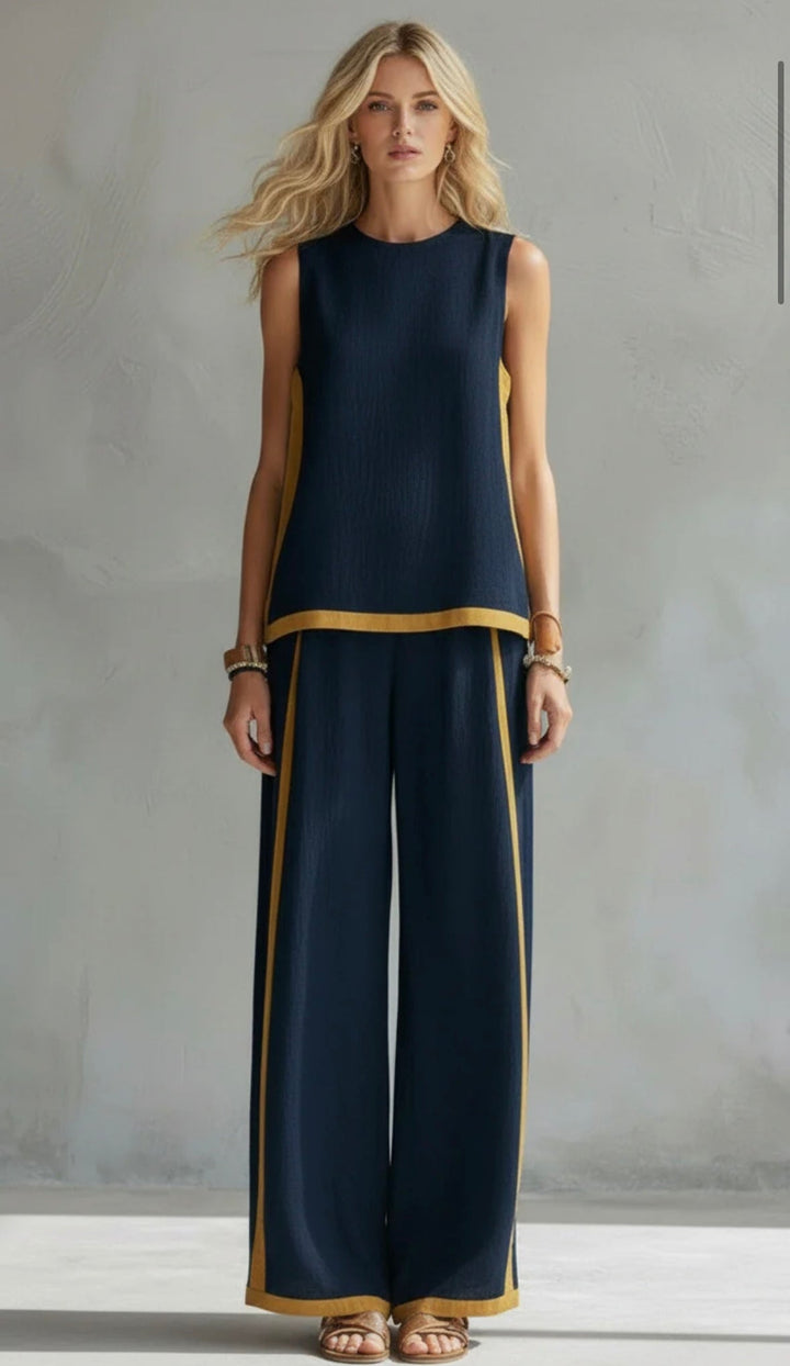 Model wearing a navy two-piece set with yellow trim, standing in front of a textured gray background.