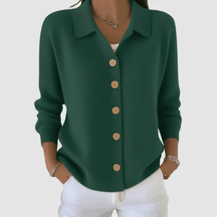 Dark green button-up knit cardigan with tan buttons, worn with white pants in a studio setting.