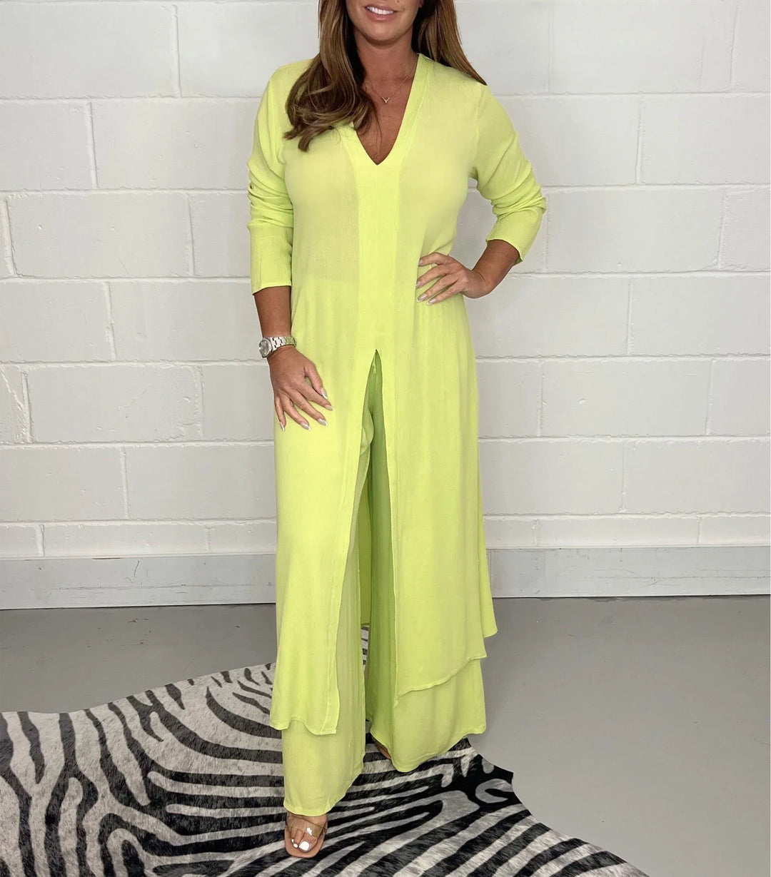 Model in a yellow two-piece set with long sleeves and a V-neck, standing on a zebra-patterned rug against a white brick wall.