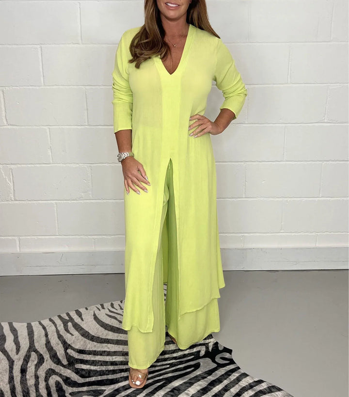 Model in a yellow two-piece set with long sleeves and a V-neck, standing on a zebra-patterned rug against a white brick wall.