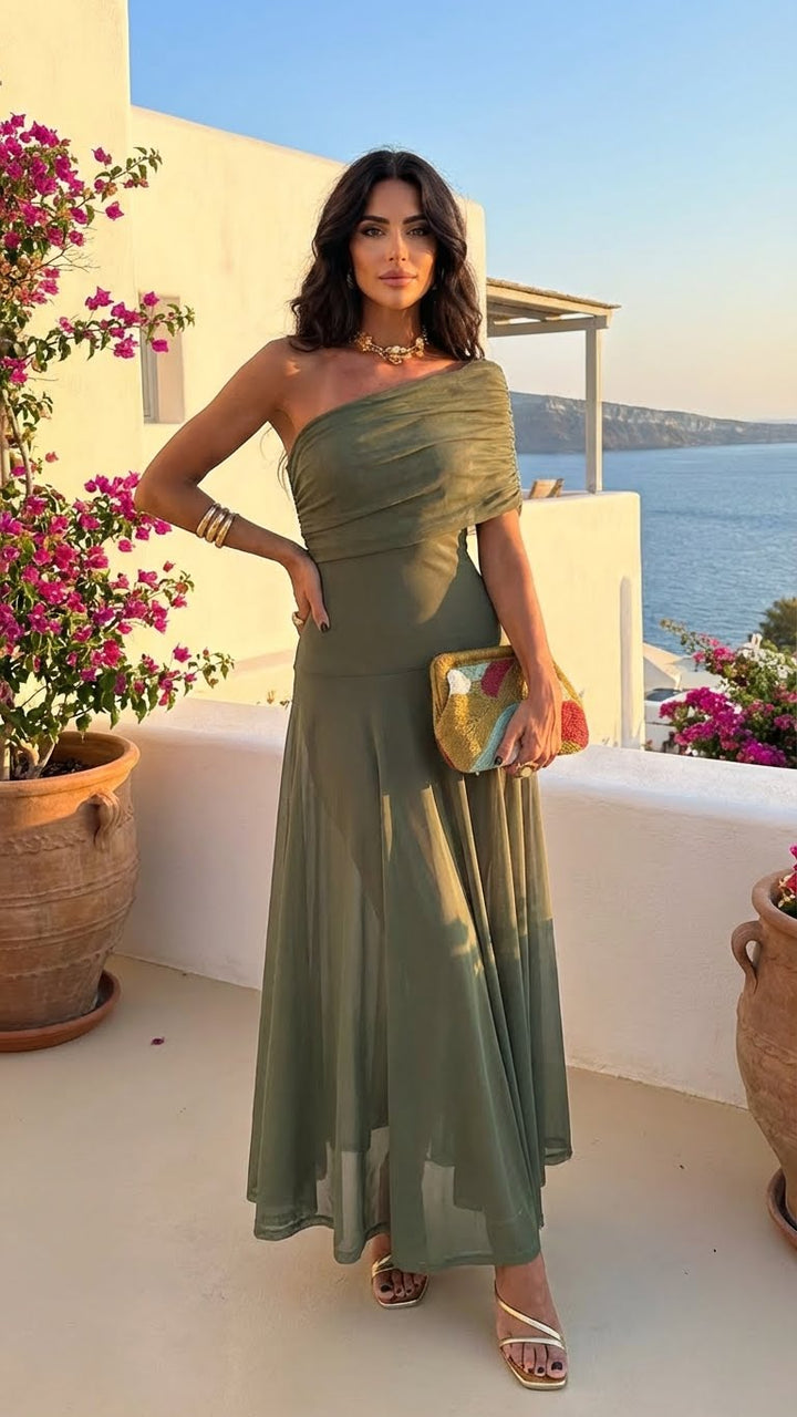 Woman in an elegant green off-shoulder dress, holding a colorful clutch, standing on a patio with potted plants and sea view.