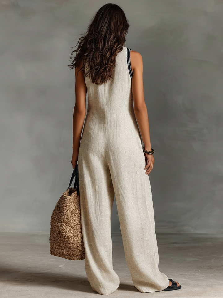 Rear view of woman in ivory jumpsuit holding a woven tote. Studio background.