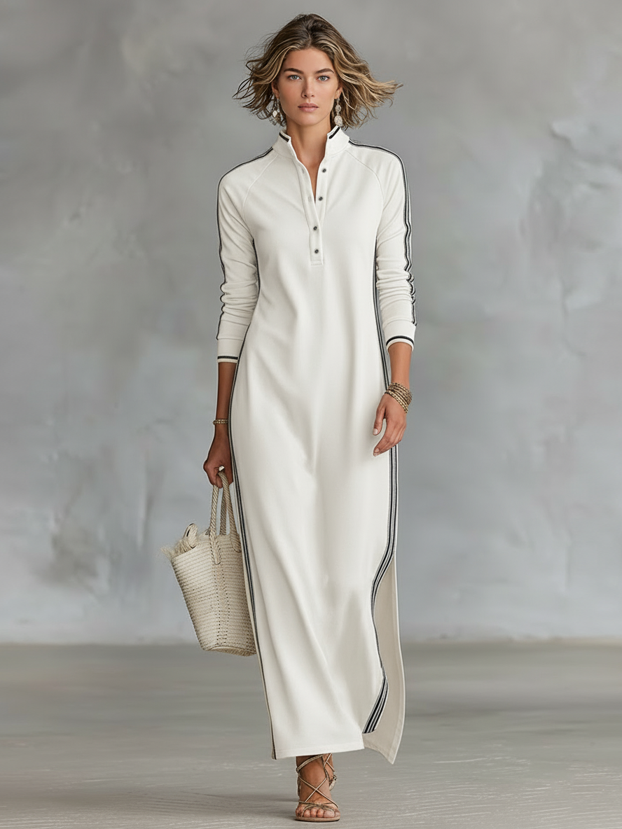 White maxi dress with dark stripes, worn by a person holding a tote. Indoor minimal background.