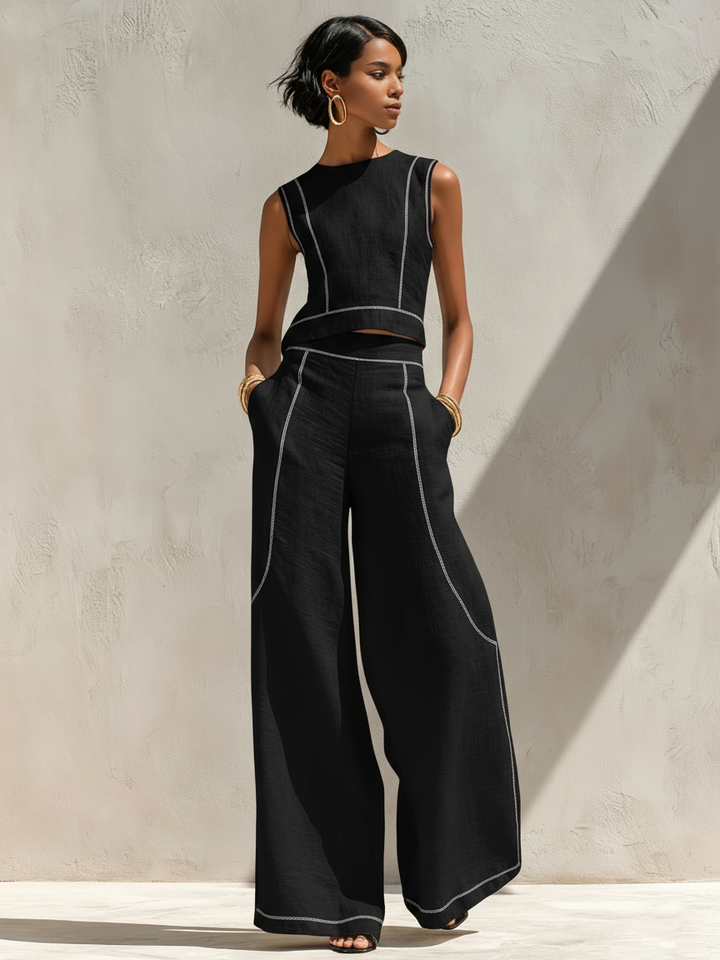 Black pants set with contrast stitching worn by woman in outdoor setting with light-colored wall.