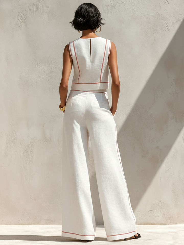 Back view of white contrast-stitched pants set, worn by woman in outdoor setting with a neutral wall.