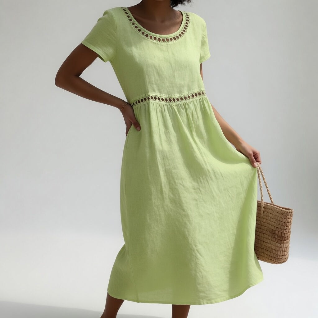 Light green midi dress featuring eyelet trim and short sleeves, worn by a person with a woven bag. Minimal studio backdrop.