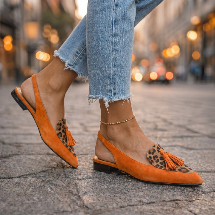 Orange leopard print sandals with tassels, worn with jeans, urban street setting.