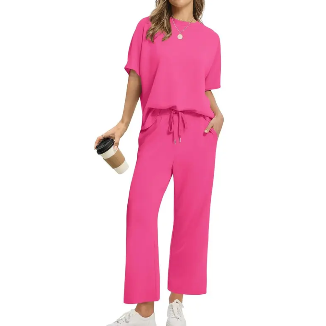 Woman dressed in a vibrant pink set with loose top and drawstring pants, holding a coffee, in a studio scene.