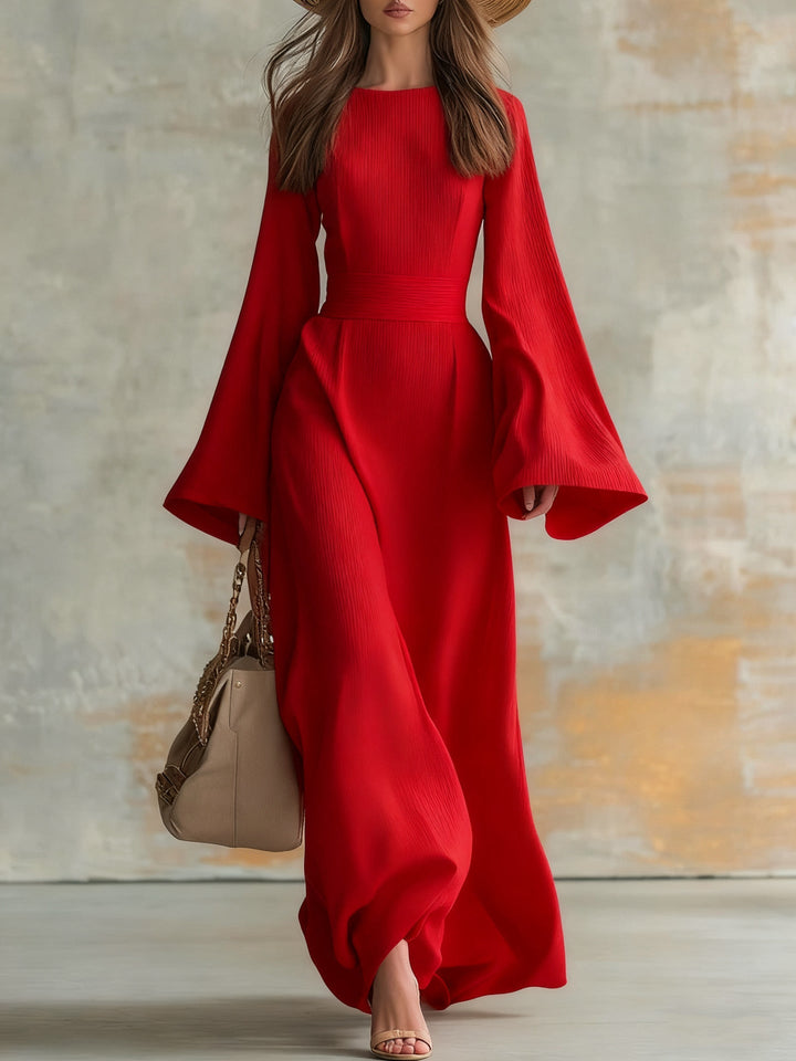 Elegant woman in a long, flowing red dress with flared sleeves, carrying a beige handbag in a studio setting.